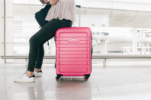 Viajera esperando vuelo apoyada en maleta rosa
